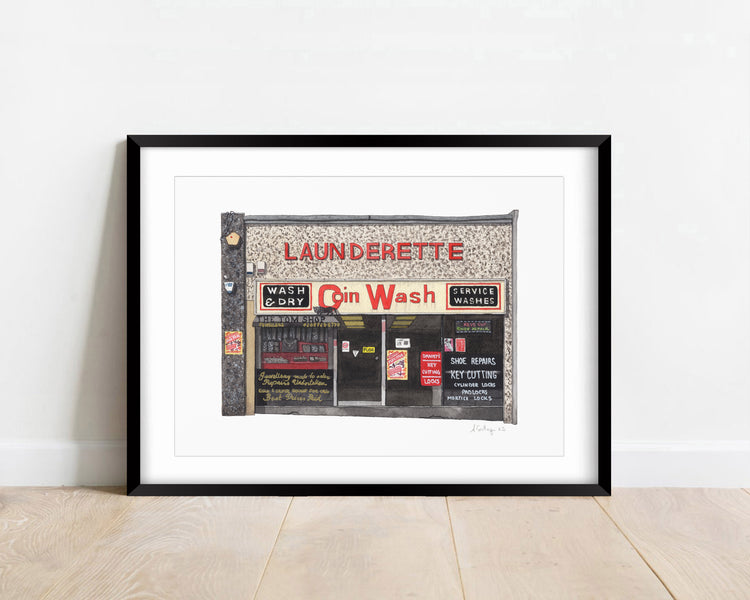 Watercolour giclée print of Coin Launderette, Streatham, shown in a black frame.