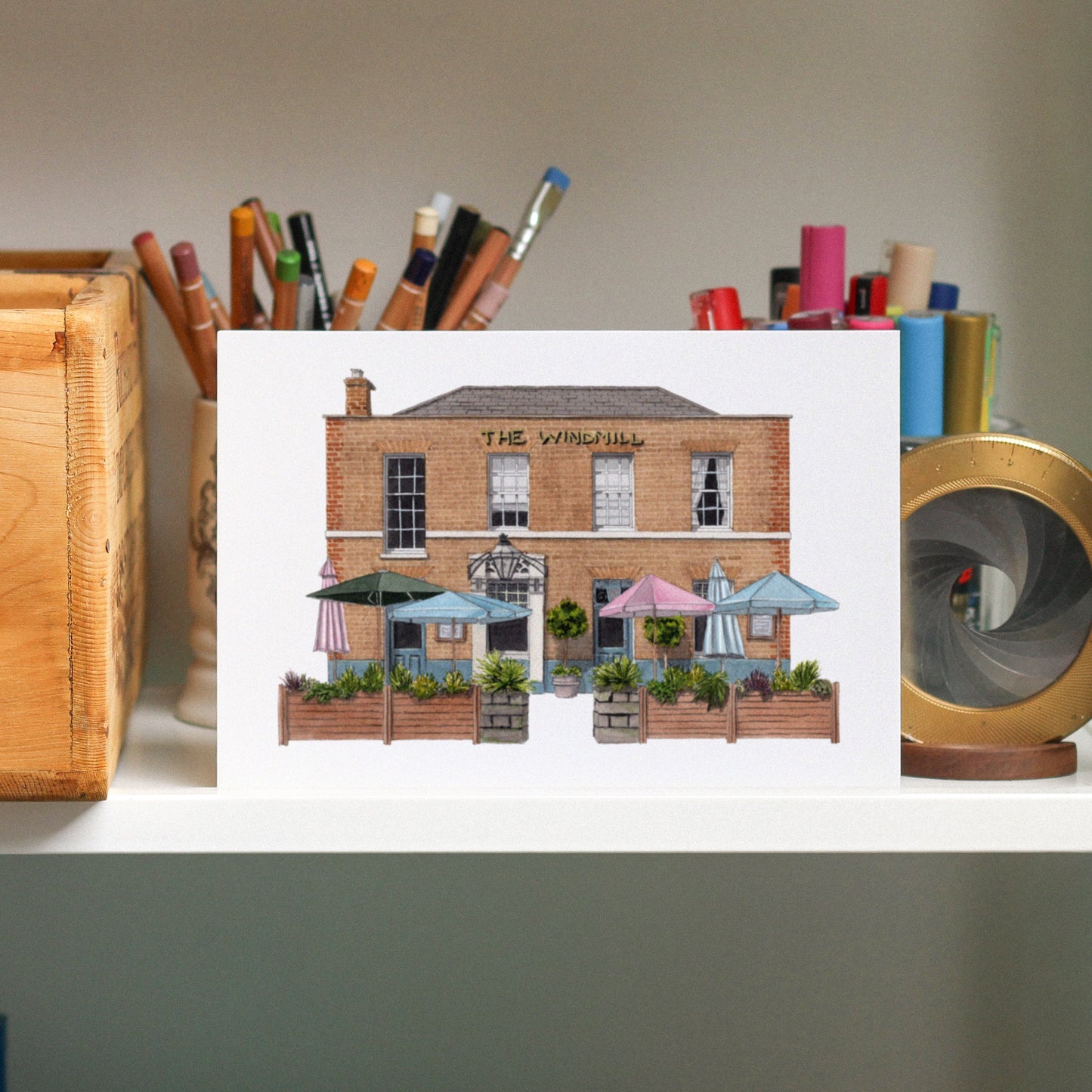 Art print of a building with outdoor seating area displayed on a surface with stationery items.