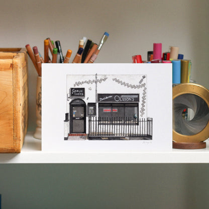 Small framed print of a building on a shelf with stationery items.
