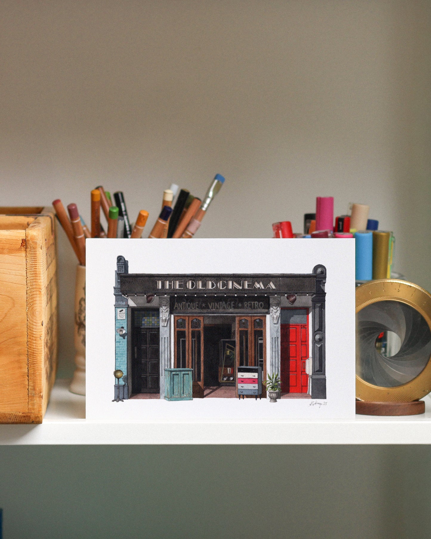 Print of THE OLD CINEMA in Chiswick displayed on a shelf with stationery items.