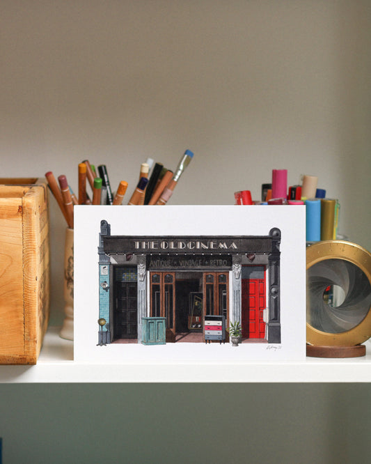 Print of THE OLD CINEMA in Chiswick displayed on a shelf with stationery items.
