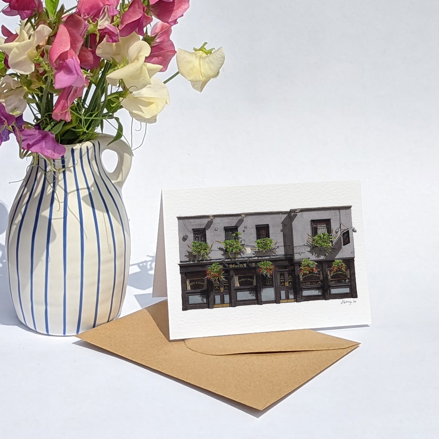 THE SEVEN STARS in Holborn greeting card is paired with a kraft paper envelope and a blue-and-white striped vase filled with pink and white sweet pea flowers.
