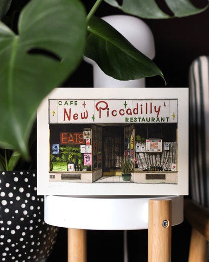 Small print of 'Cafe New Piccadilly' design on a stand with plants in the background