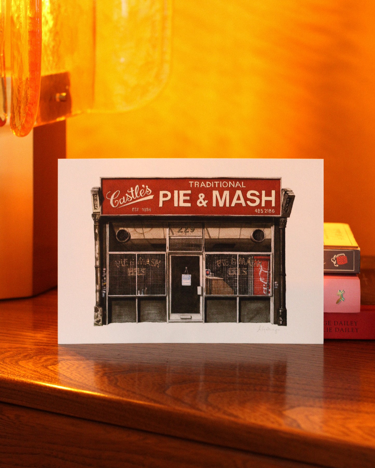Print of Castle's a pie and mash shop design on a wooden surface with a warm glow.