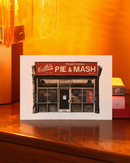 Print of Castle's a pie and mash shop design on a wooden surface with a warm glow.