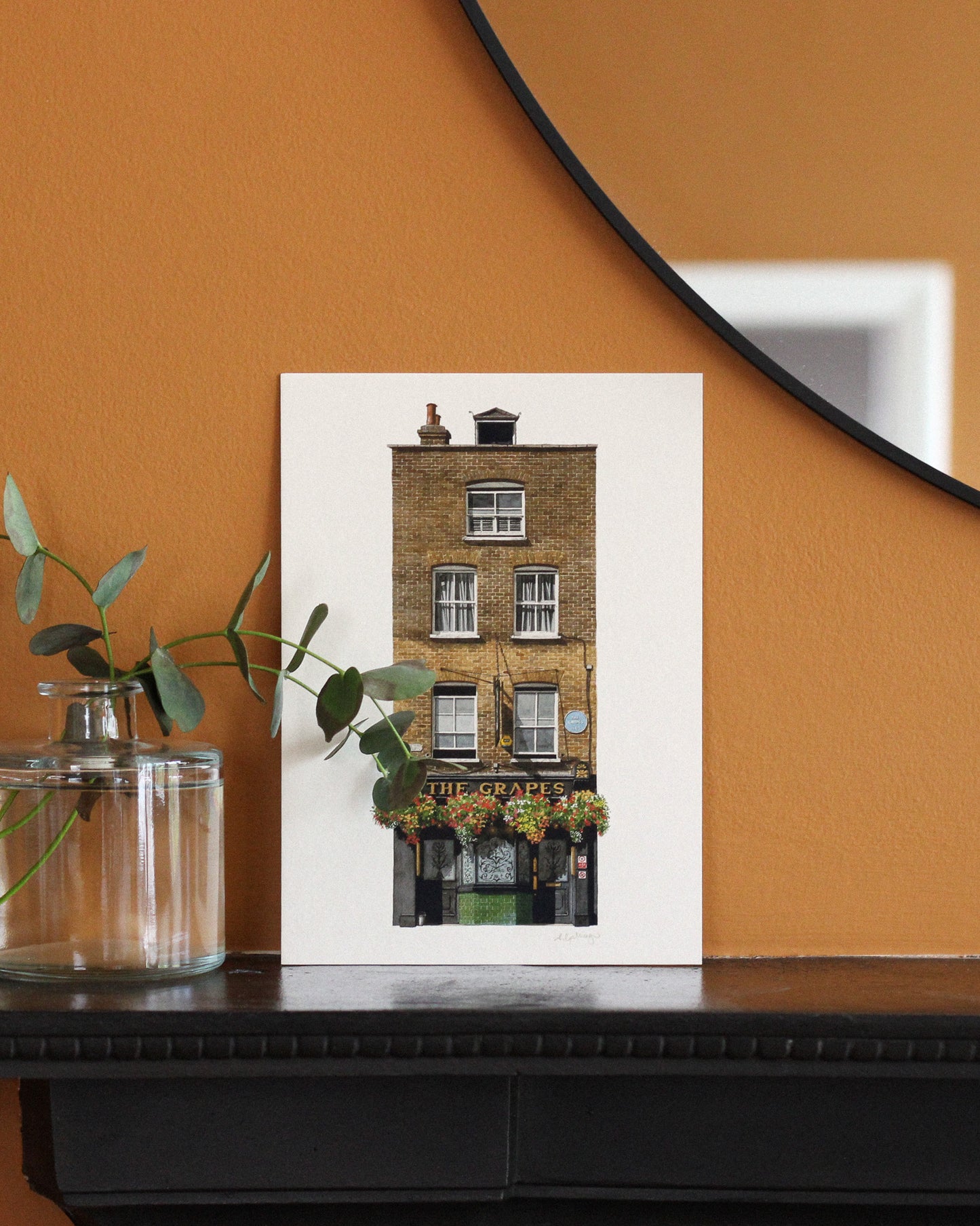 Framed print of The Grapes on an orange wall with a plant and mirror.