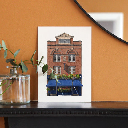 Framed print of a brick building with blue awnings on an orange wall.