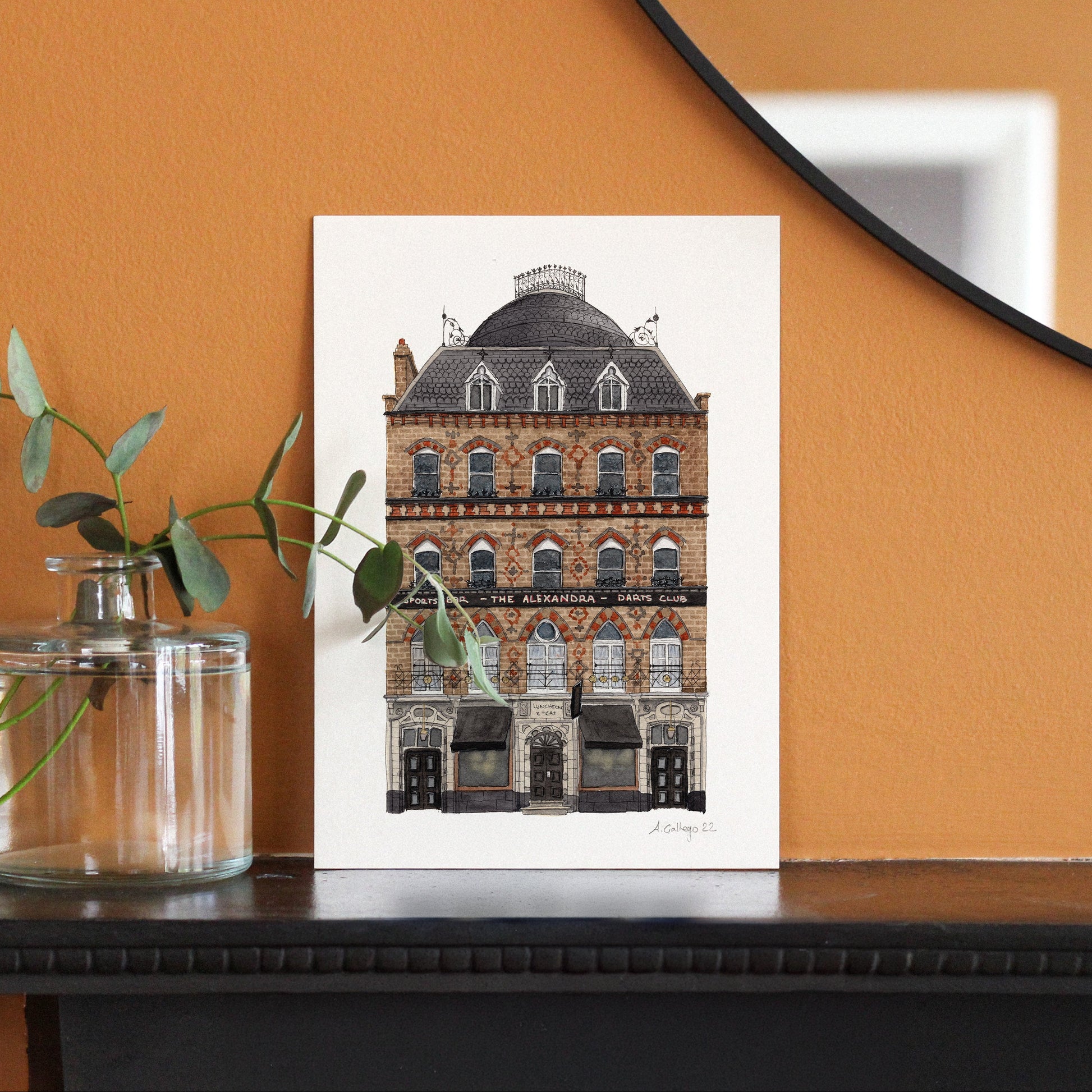 Framed artwork of a building on a wooden surface with an orange wall background