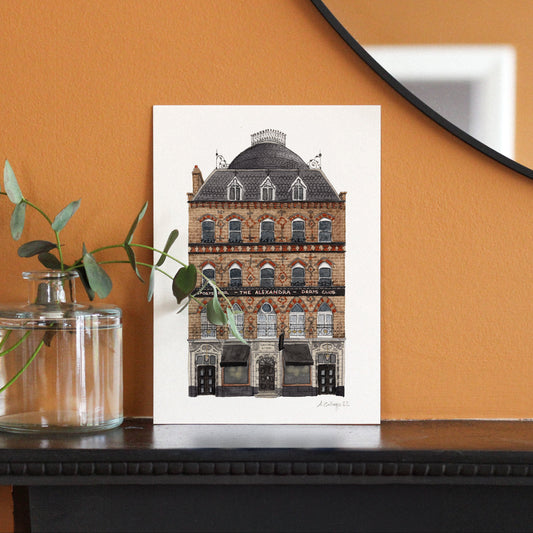 Framed artwork of a building on a wooden surface with an orange wall background