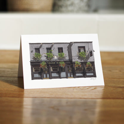 A close-up, low-angle shot of THE SEVEN STARS in Holborn greeting card standing independently on a polished wooden floor, showing the card's sturdy fold and matte finish.