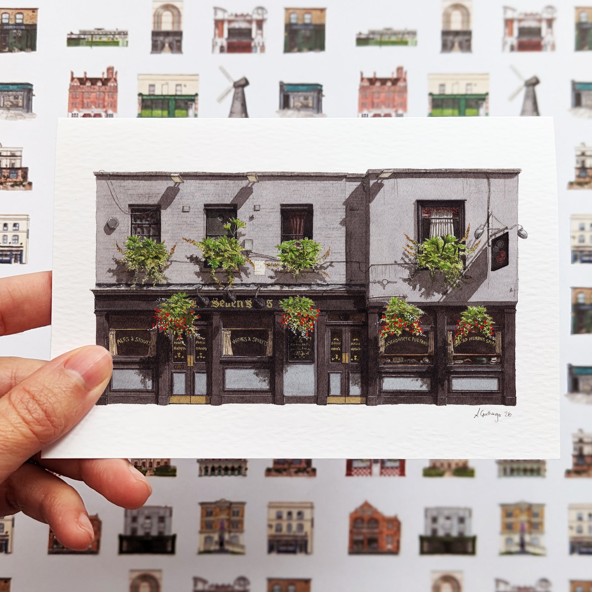 A hand holds the THE SEVEN STARS in Holborn greeting card against a background of matching London-themed wrapping paper, showcasing a complete gift-wrap set.