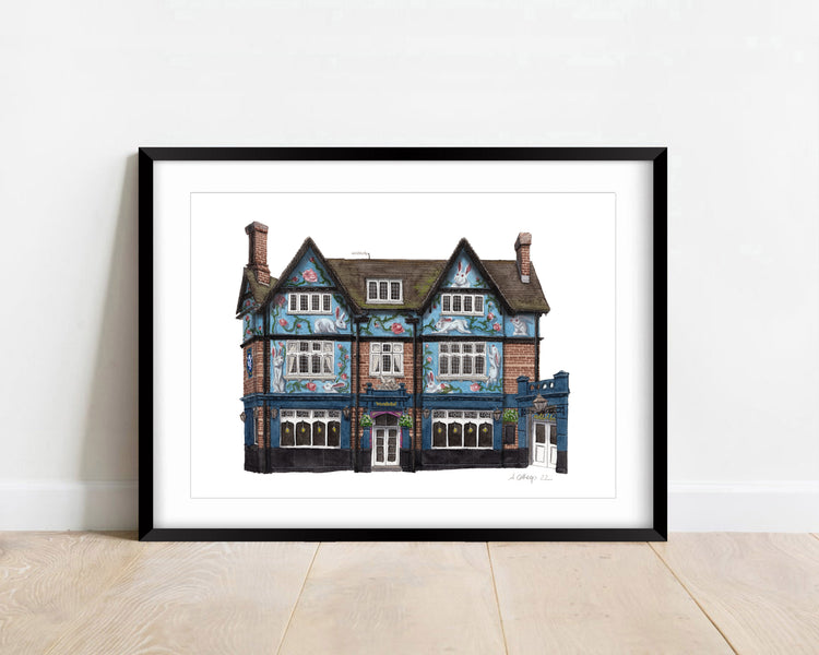 Watercolour giclée print of The Rabbit Hole pub, Streatham, shown in a black frame against a white wall.